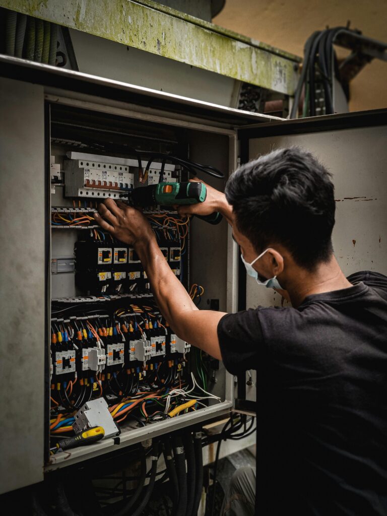 pexels-photo-9679179-9679179 Technician working on circuit breaker panel, adjusting electrical wires indoors.
